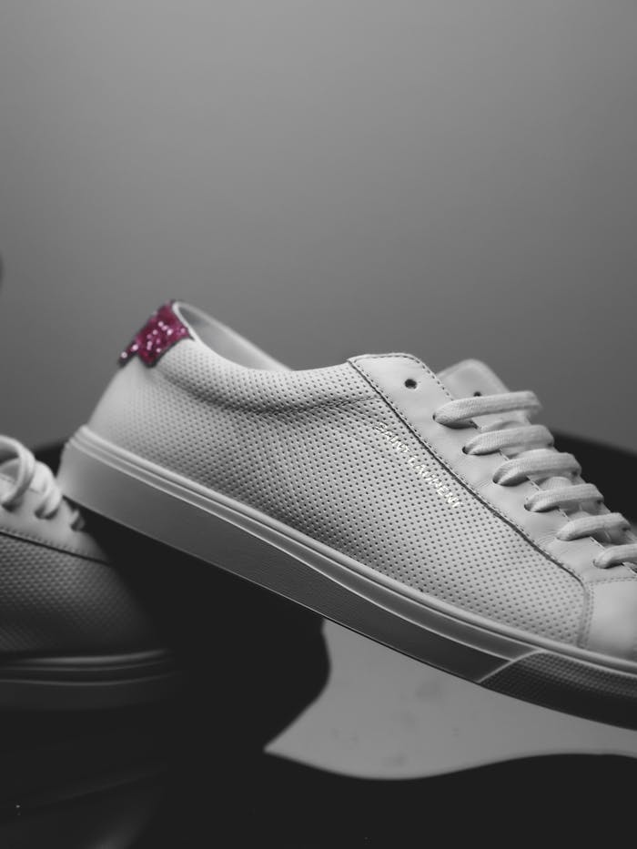 Close-up of elegant white sneakers with perforated texture and pink accent.