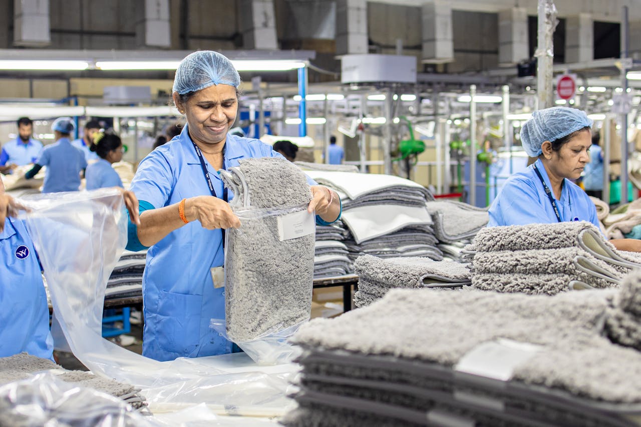 Indian factory workers sorting gray rugs in a textile manufacturing setting.