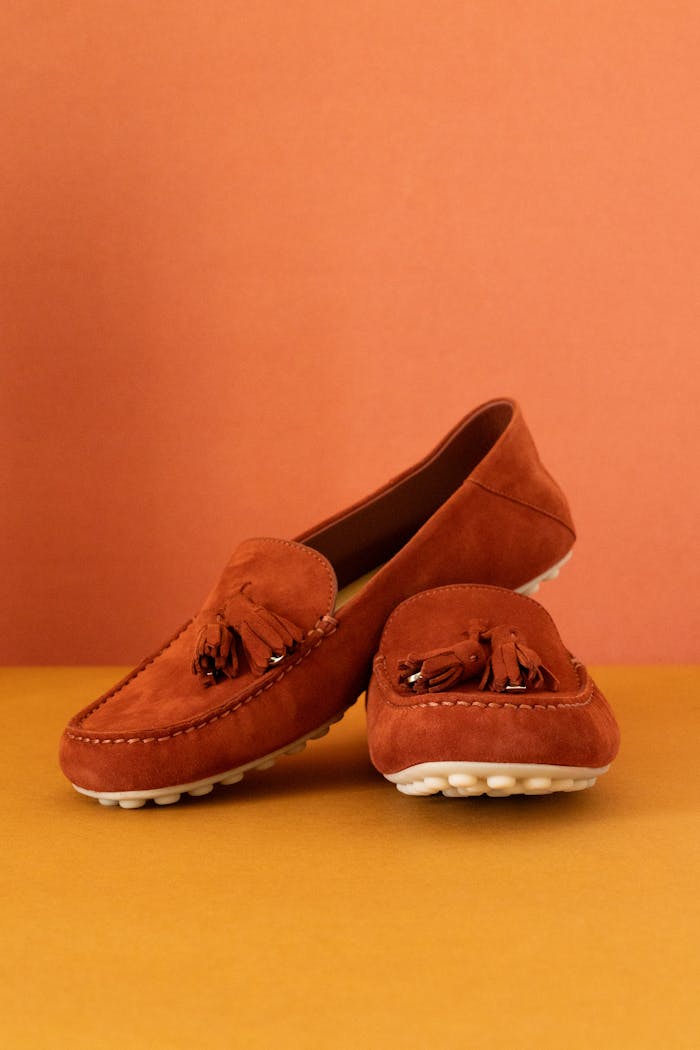 Stylish brown suede loafers with tassels on colored background.